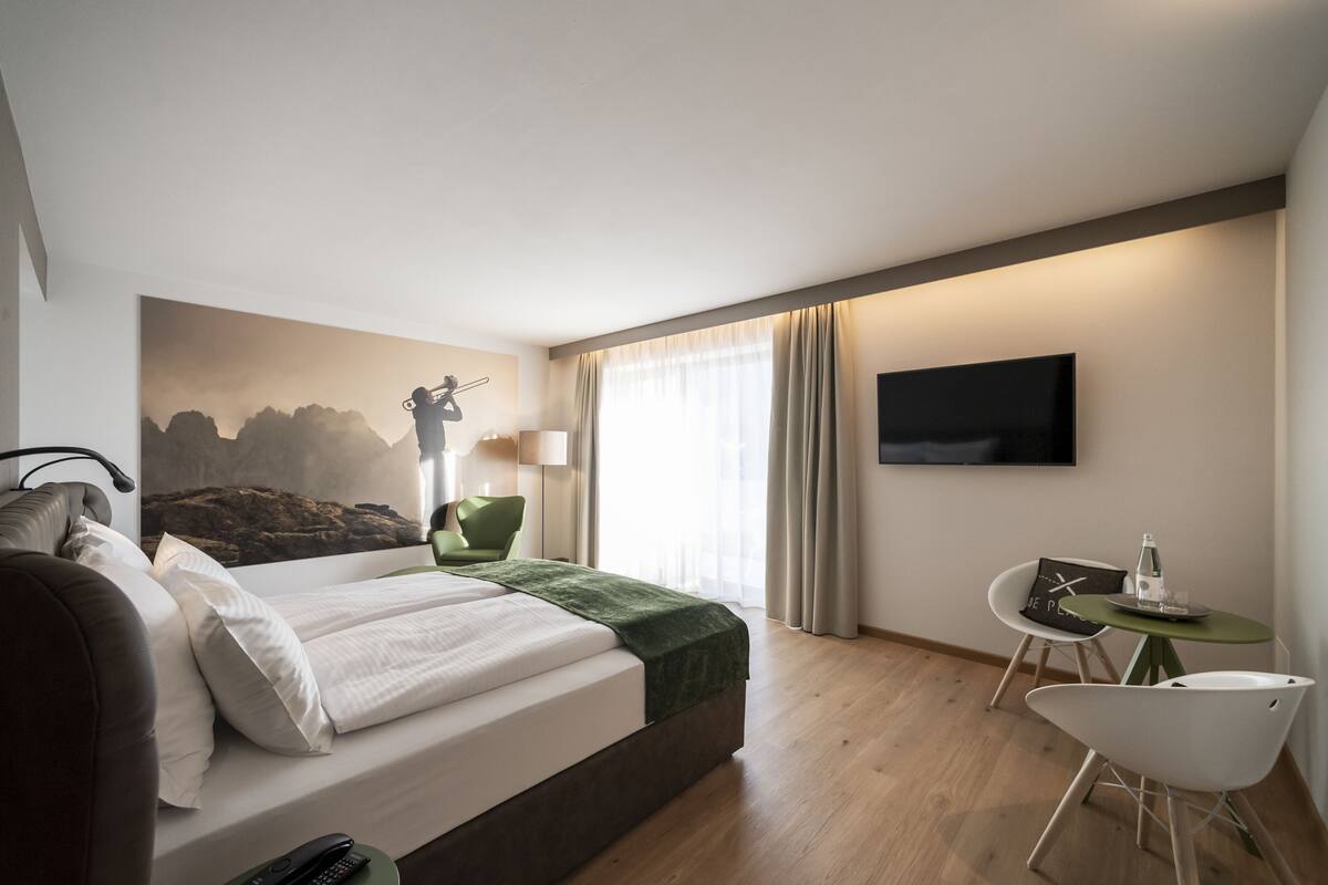 Une chambre d’hôtel moderne, équipée d’un lit, d’un bureau, d’une chaise, d’une télévision et d’un tableau au mur.