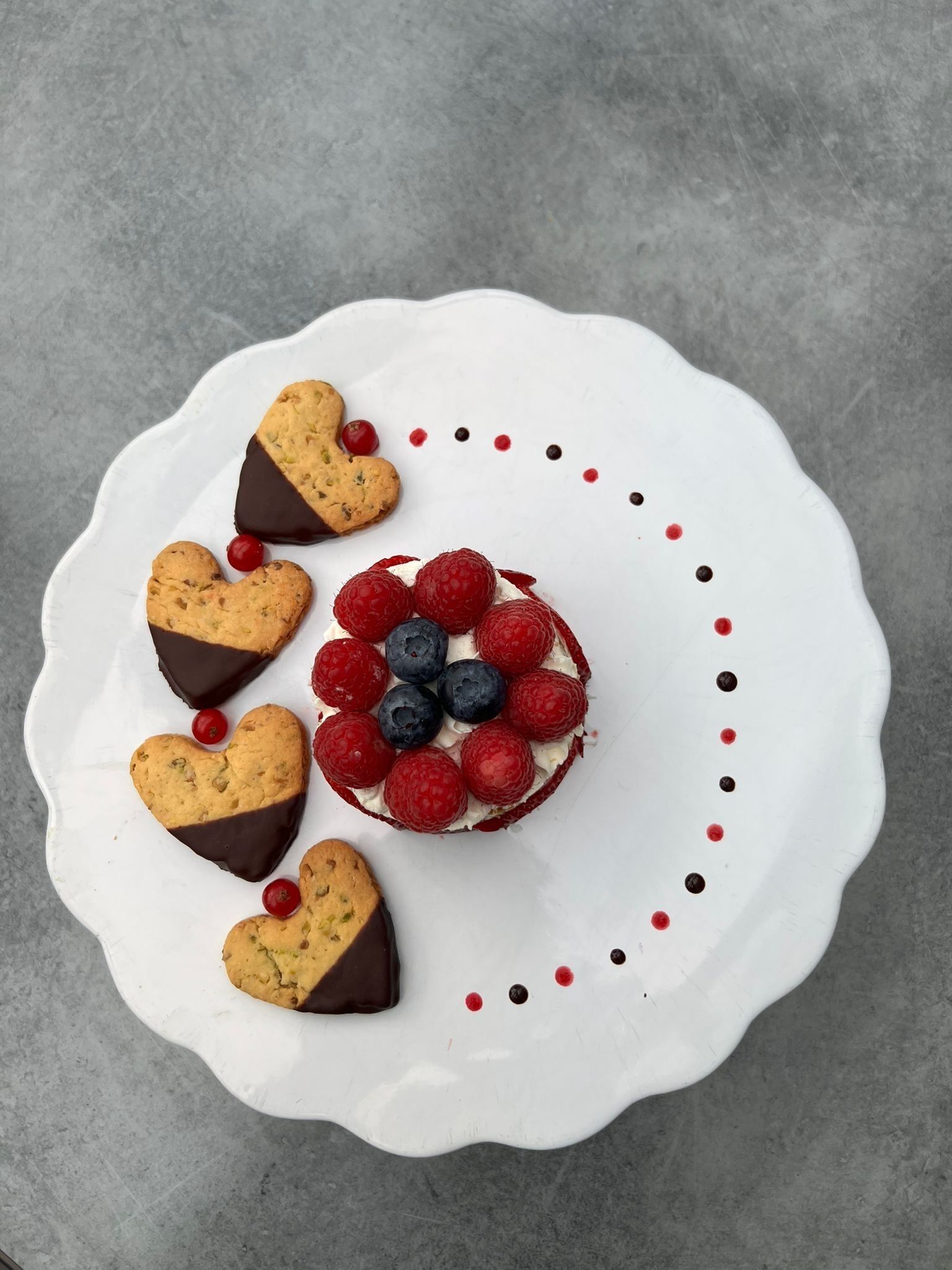 Une assiette blanche sur laquelle est présentée une pâtisserie décorée de biscuits en forme de cœur et surmontée de fruits rouges.