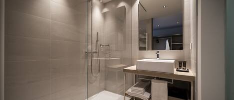 A modern bathroom with a glass-enclosed shower, a white sink, and a large mirror.