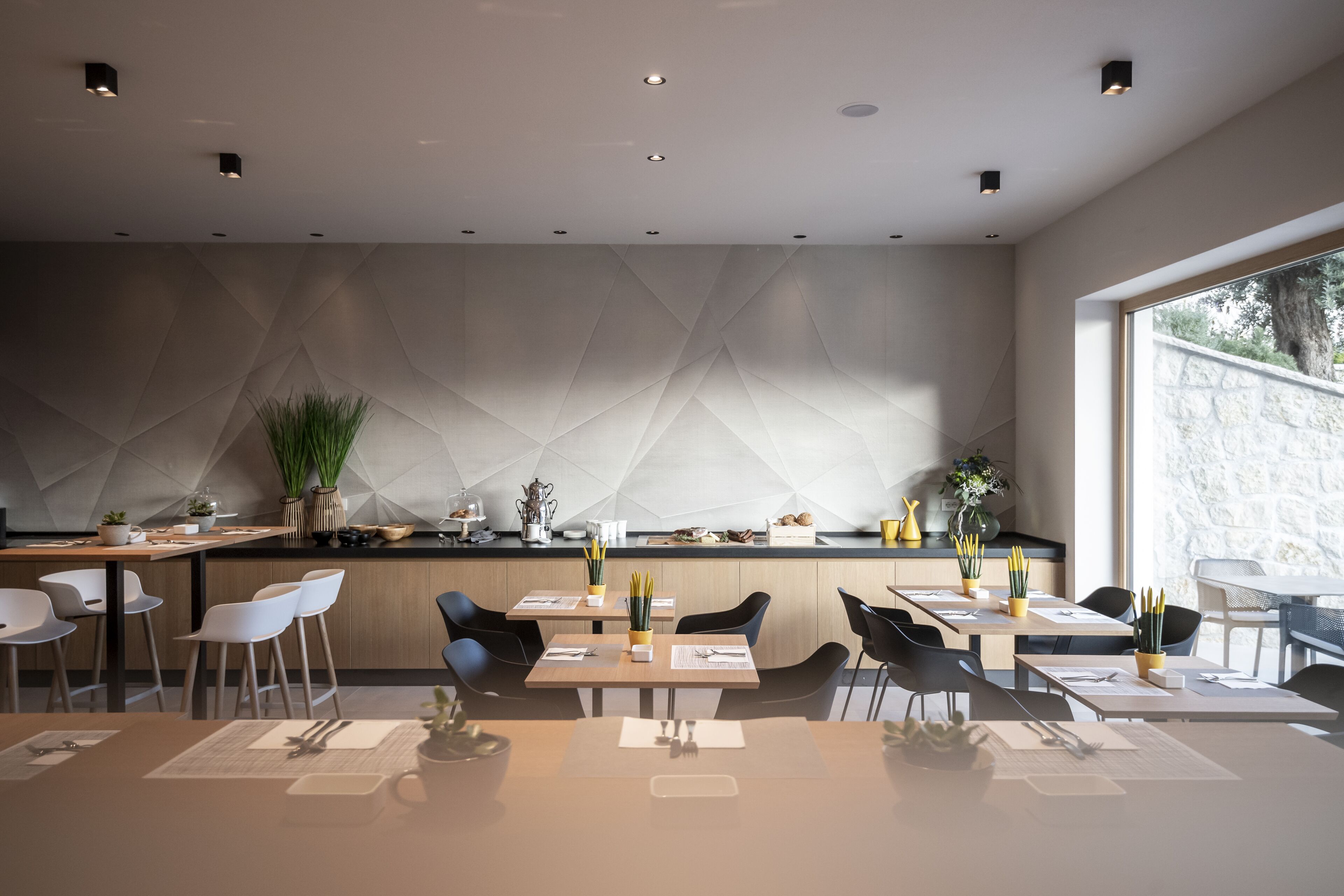 A modern dining area with a geometric wall design, wooden tables, and chairs.