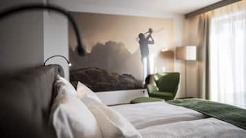 Habitació d'hotel amb un llit, una cadira verda, una làmpada i una paret amb una pintura de muntanya.