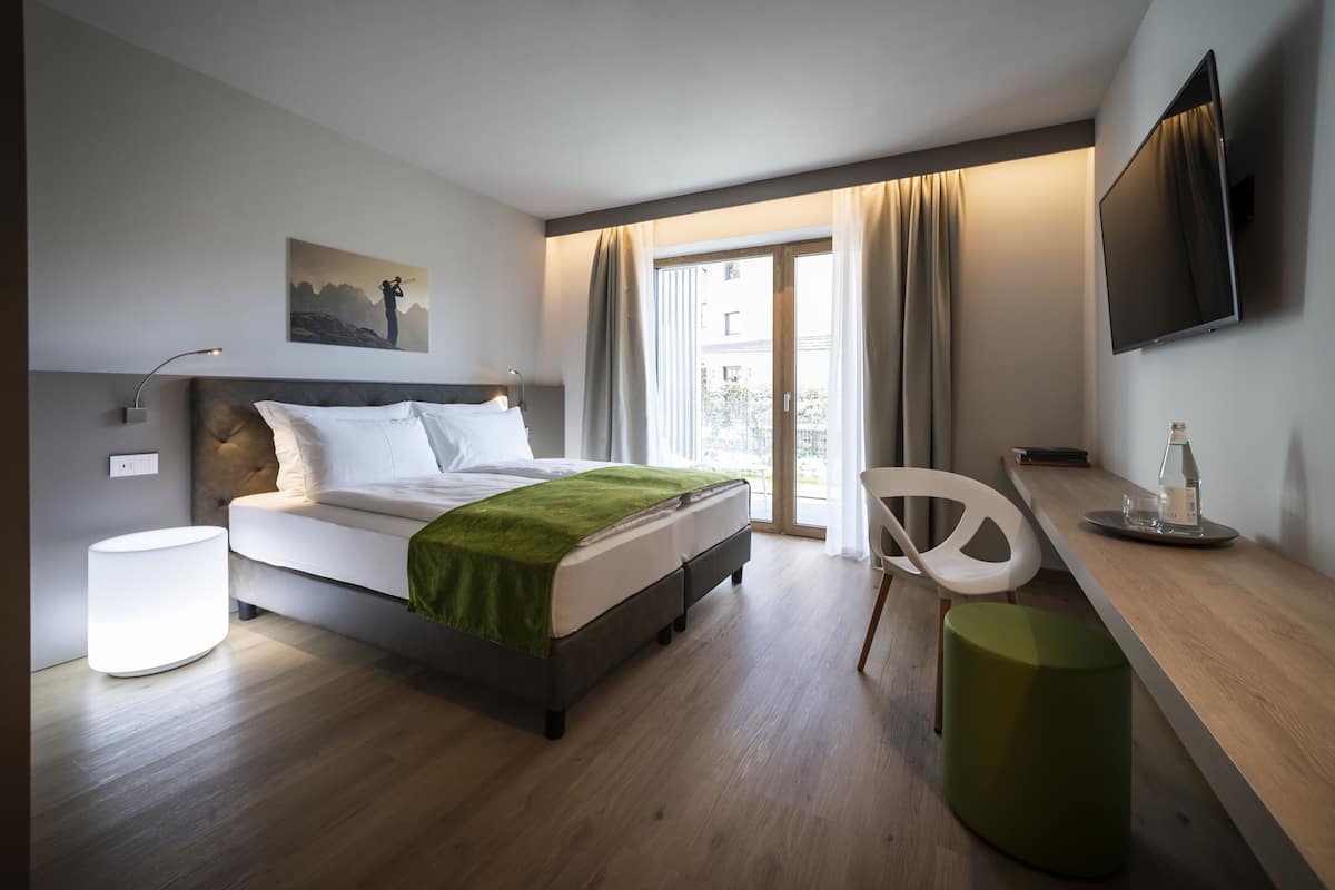 Une chambre d’hôtel moderne équipée d’un lit, d’une table de chevet, d’une chaise et d’un téléviseur fixé au mur.