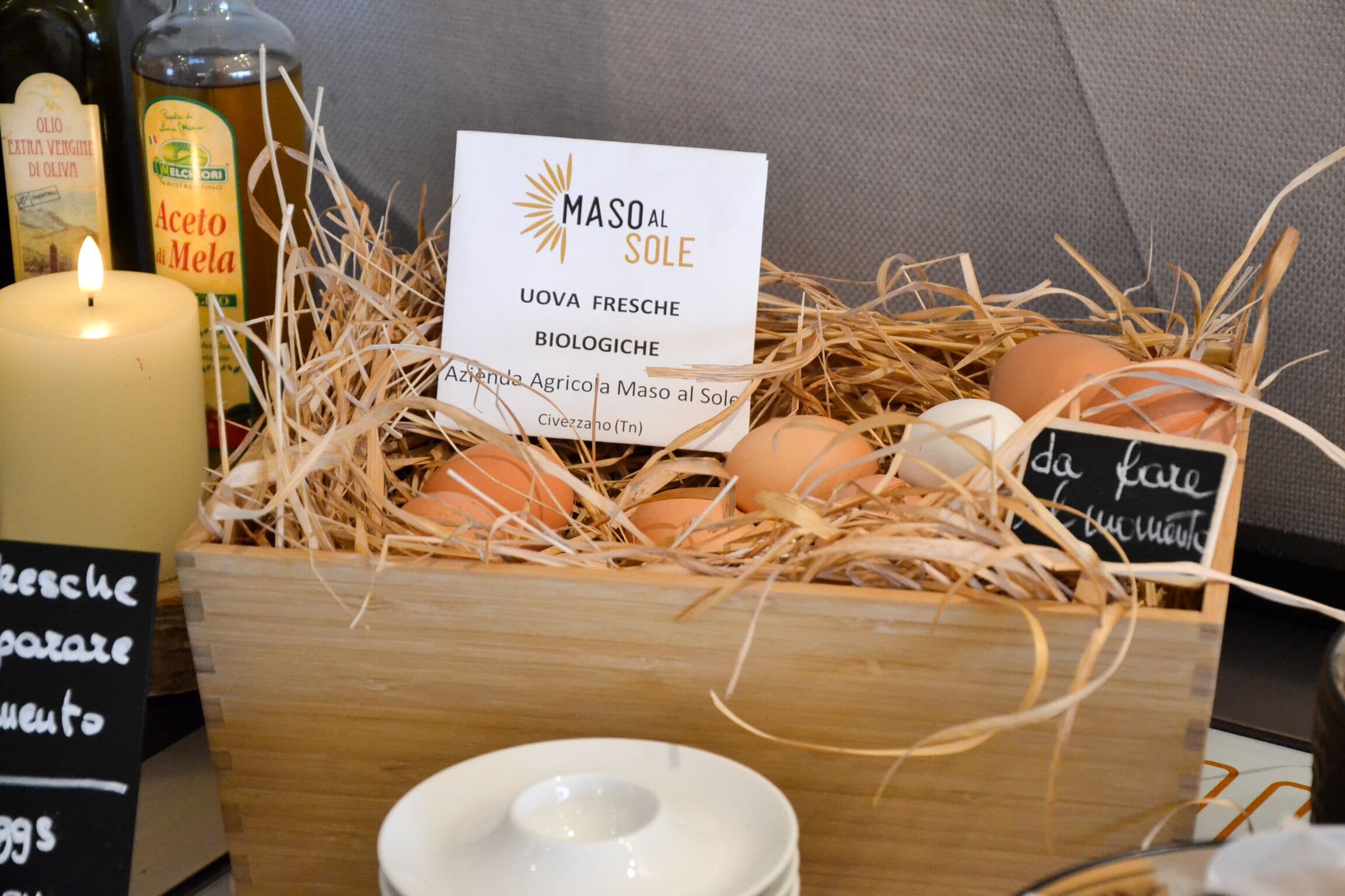 Ein hölzerner Korb voller Eier, eine brennende Kerze und ein Schild mit der Aufschrift 'Maso al Sole Uova Fresche Biologiche'.