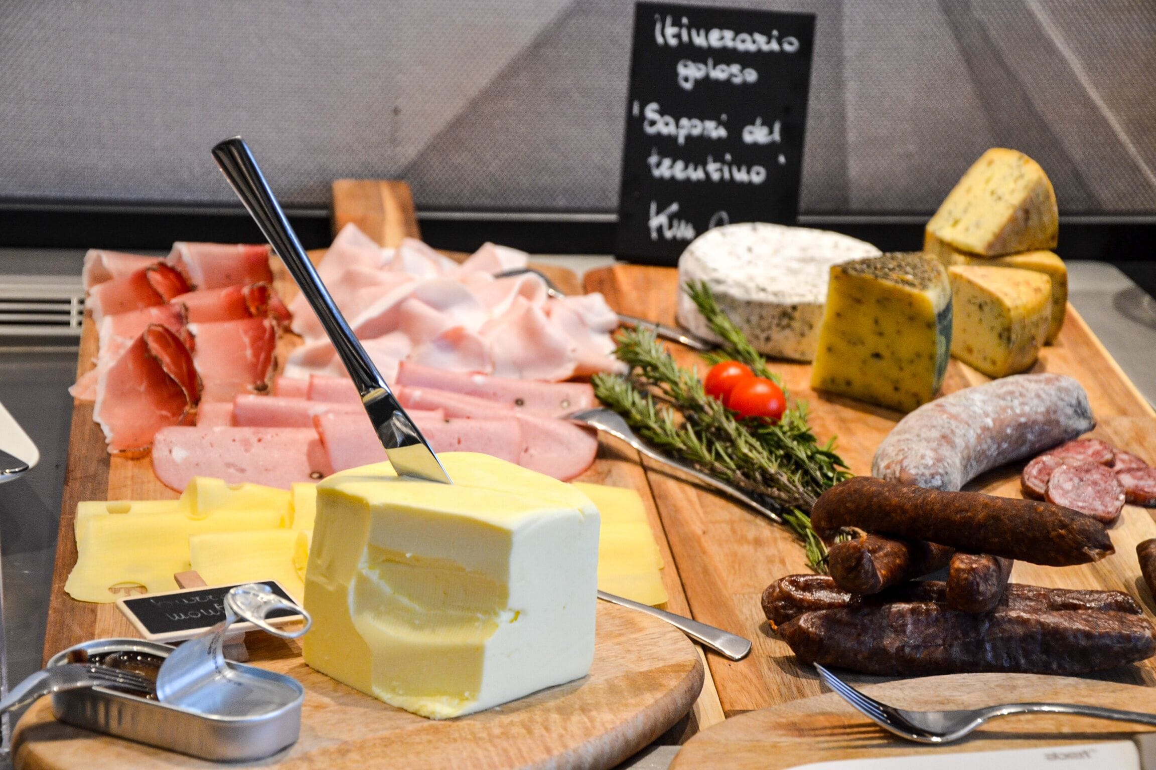 A variety of cheeses, cured meats, and a sign indicating a selection of gourmet items.