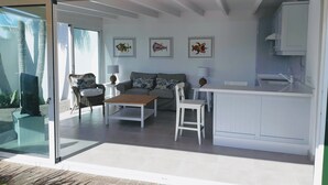 Een moderne woonkamer met een bank, salontafel en stoelen, een keukenhoek met een eettafel en kunstwerken aan de muur.