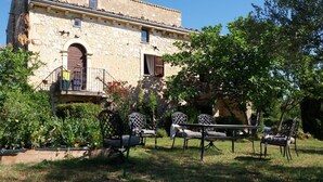 Un edificio in pietra con un balcone, immerso in un giardino ricco di piante e arredi da esterno.