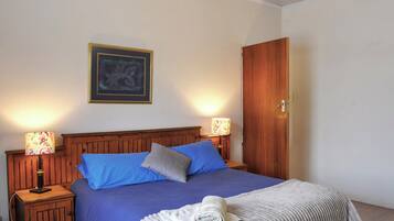 Cama bem arrumada com almofadas azuis e cinzas, cabeceira de madeira e uma obra de arte emoldurada acima.