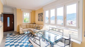 Un salon avec un sol à carreaux, une table à plateau en verre, un canapé et une vue sur les montagnes grâce à de grandes fenêtres.