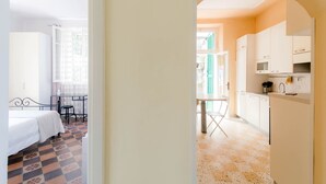 Une pièce comprenant un lit, une petite table et une chaise. Il y a également un coin cuisine avec des placards et un plan de travail.