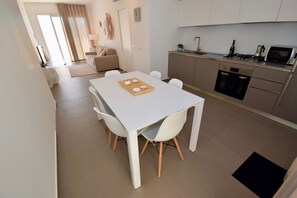 A modern kitchen with a dining area, including a table with chairs and a wooden board with food items. - Casa Blanca Villa Superior (Marina di Ragusa)