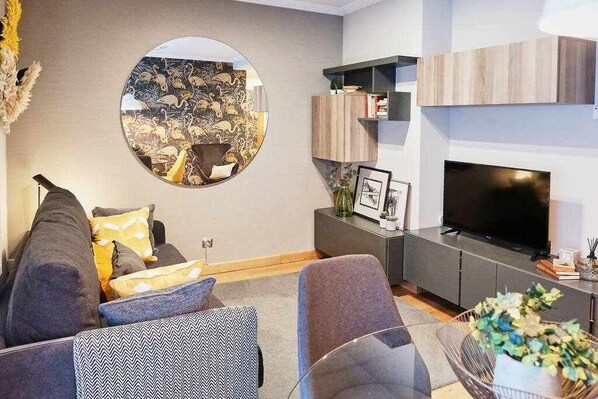 A modern living room with a round mirror, grey sofa, and a flat-screen TV.