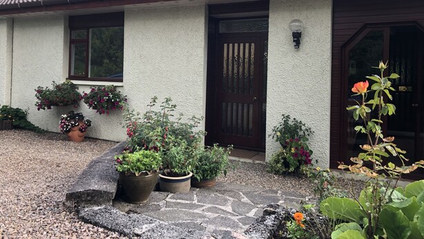 Une maison avec un toit recouvert de tuiles, une porte d’entrée et des plantes en pot disposées autour de l’entrée.