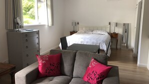 Une chambre à coucher comprenant un lit, des tables de chevet, une commode, un canapé avec des coussins rouges et une fenêtre avec des rideaux.
