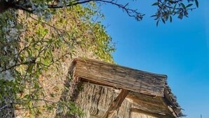 Ett rustikt utomhuskök med en stenugn, en träpergola och en stenmur.