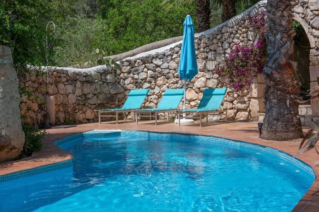 A swimming pool with stone walls and lounge chairs.