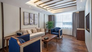 Ein modernes Wohnzimmer mit einer Couch, Sesseln, einem Couchtisch und einem großen Fenster mit Vorhängen.
