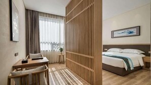 Ein Hotelzimmer mit einem hölzernen Bett, einem Schreibtisch mit Stuhl, einem kleinen Tisch und einem großen Fenster mit Vorhängen.