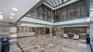 Eine großzügige Lobby mit Fischgrätparkett, einer Rezeption, einer Sitzecke und einem großen Fenster mit dekorativen Gitterstäben.