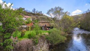 A rustic stone house with a thatched roof, situated beside a flowing river, surrounded by lush greenery and trees. - Casa Rural Aguas Frías I, II y III for 2 people (Riello)
