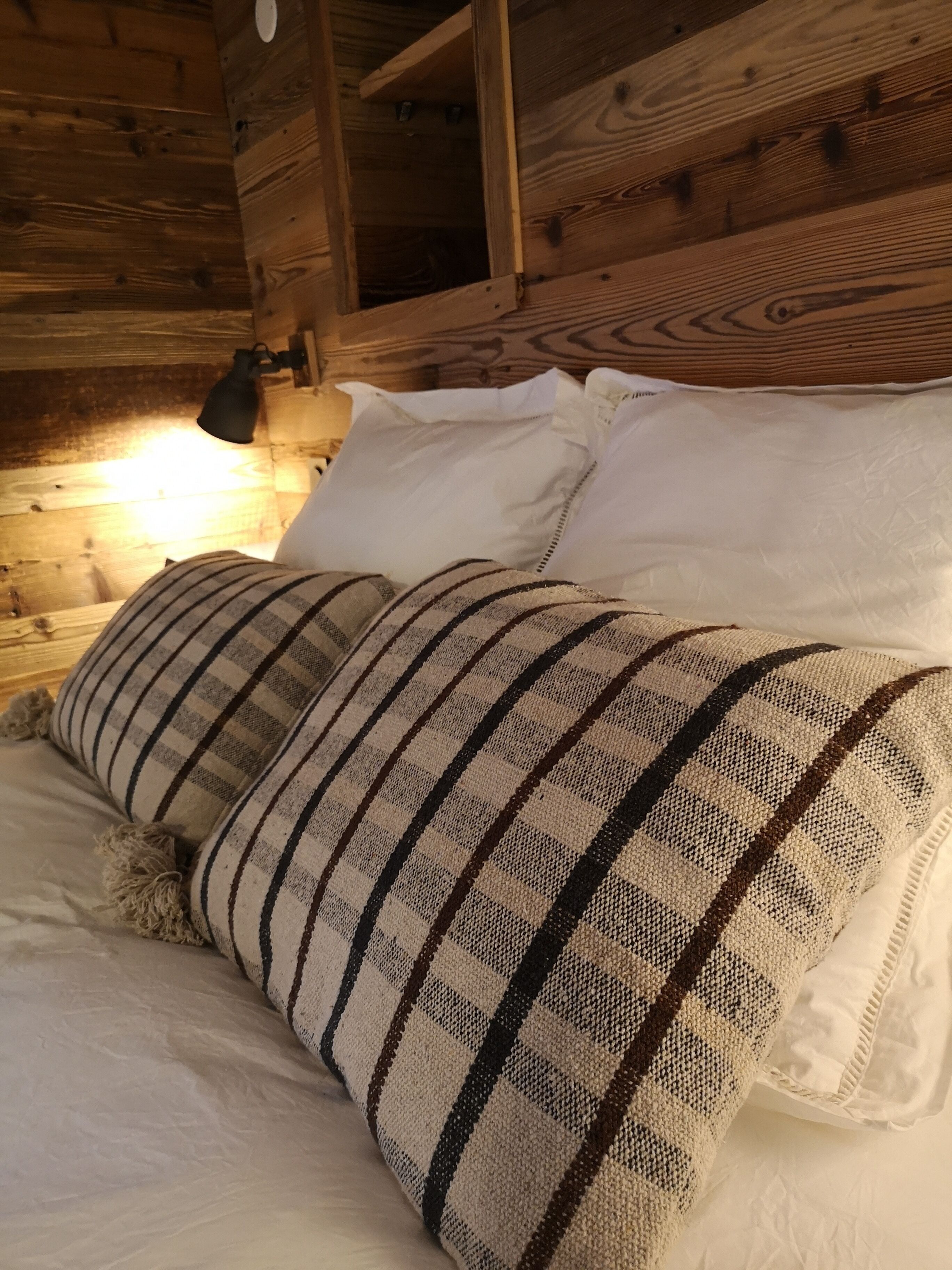 A wooden cabin interior with a bed featuring a striped blanket and white pillows.