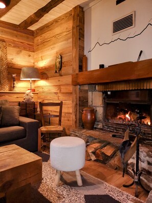 Een knus interieur met een open haard, houten wanden, een bank, een lamp en een vloerkleed.