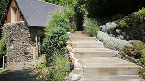 Un escalier en pierre mène à un chalet en bois doté d’un toit en pente, qui est entouré d’une végétation luxuriante et de plantes en fleurs.
