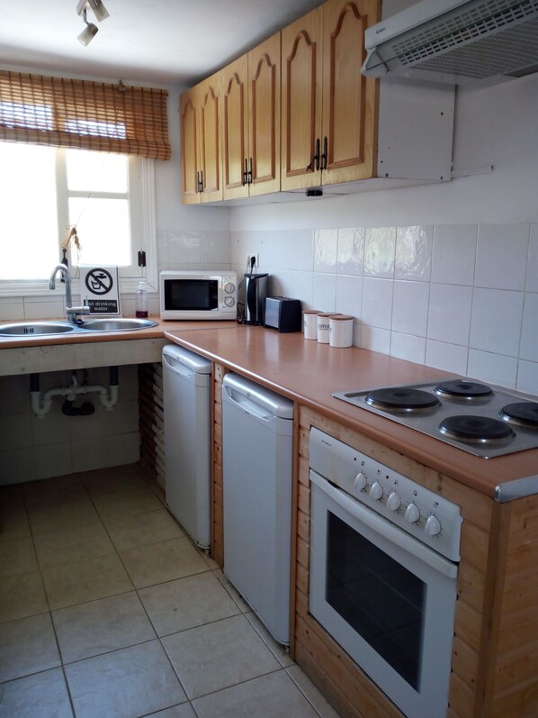 Kitchen features a dishwasher, microwave, toaster, and stove with four burners, along with wooden cabinetry and a tiled floor.