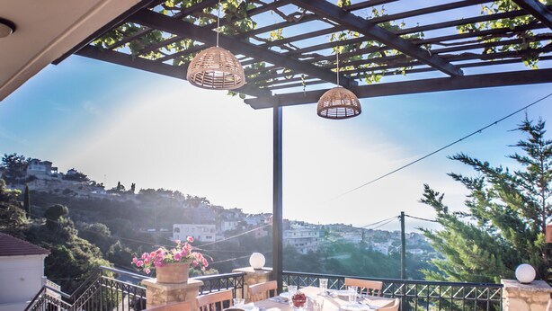 A terrace with a table set for dining, a pergola with hanging lights, and a view of a hillside. - Charmful villa, stunning views,pool, hot tub & BBQ (Roussospiti)