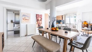 A modern living space with a dining area, a bench, a table with fruit, and a kitchen in the background. - Charmful villa, stunning views,pool, hot tub & BBQ (Roussospiti)