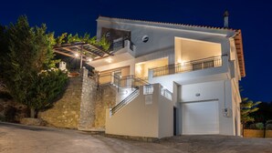 A two-story building with a garage, a staircase with railings, and a stone wall. - Charmful villa, stunning views,pool, hot tub & BBQ (Roussospiti)