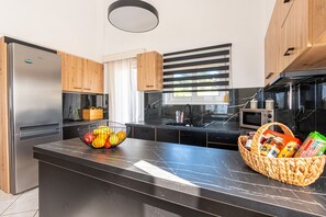 A modern kitchen with a stainless steel refrigerator, wooden cabinets, a marble countertop, a black sink, and a window with blinds. - Charmful villa, stunning views,pool, hot tub & BBQ (Roussospiti)