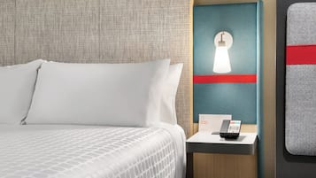 A hotel room with a bed, a nightstand with a phone, and a wall-mounted light fixture.