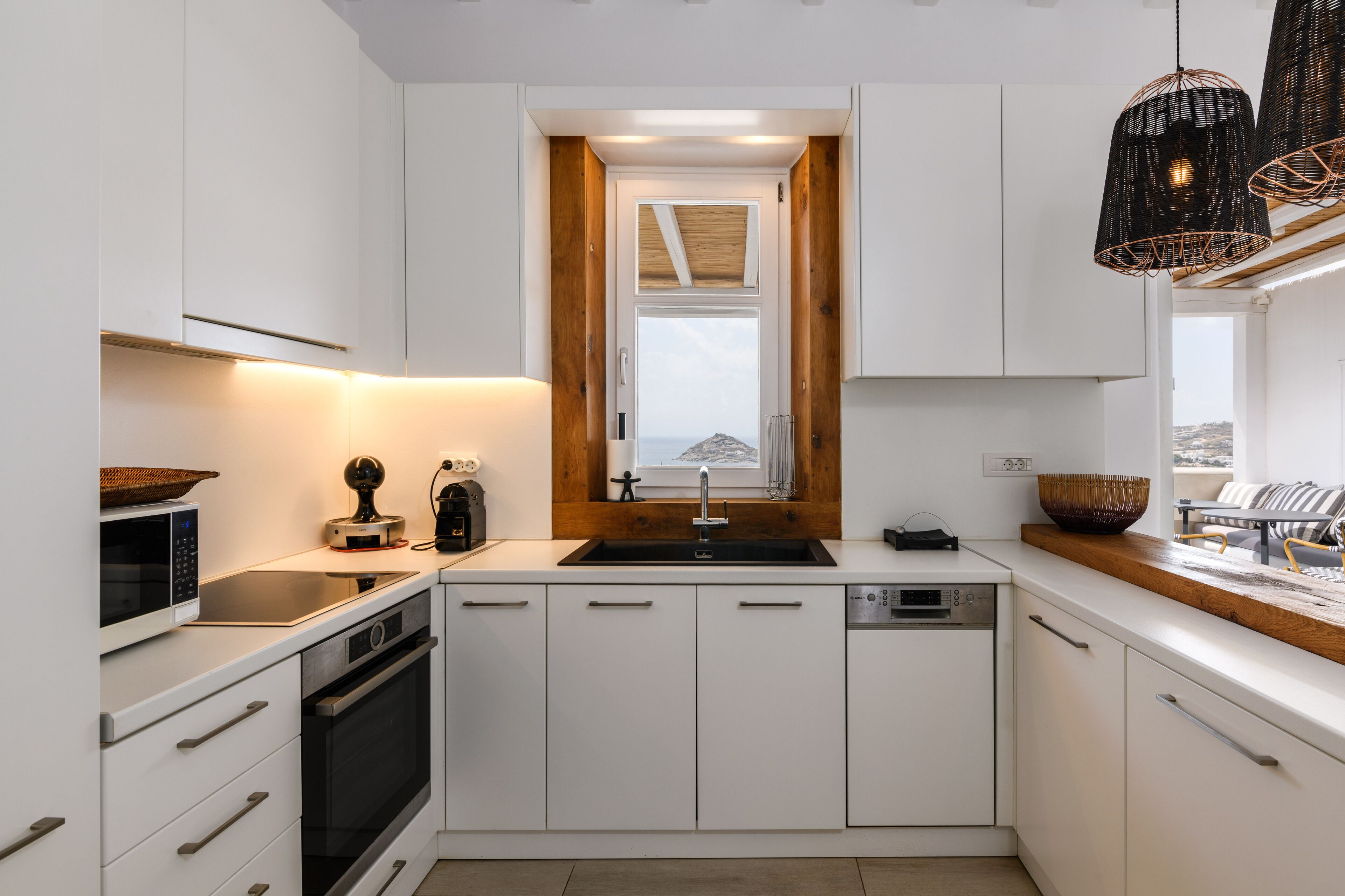 Eine moderne Küche mit weißen Schränken, einer Holz Arbeitsplatte, einem schwarzen Spülbecken und einem Fenster darüber.