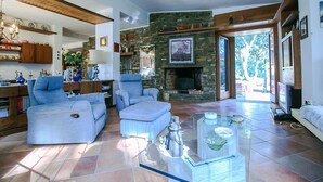 Ein Wohnzimmer mit Kamin aus Stein, blauen Sofas und einem Glastisch.