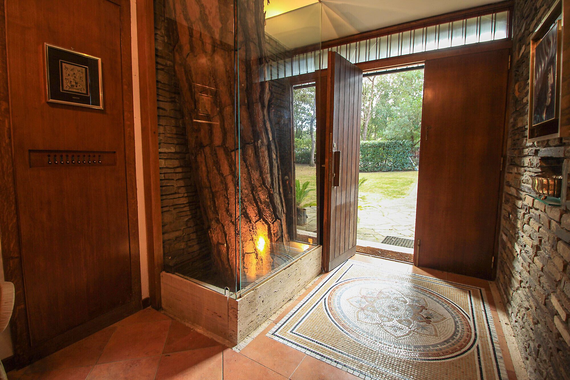 Une porte en bois ornée d’un tableau encadré, un mur de pierre et une porte vitrée donnant sur l’extérieur.