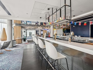 Un'area bar moderna con un lungo bancone, sgabelli bianchi e una selezione di bottiglie sugli scaffali.
