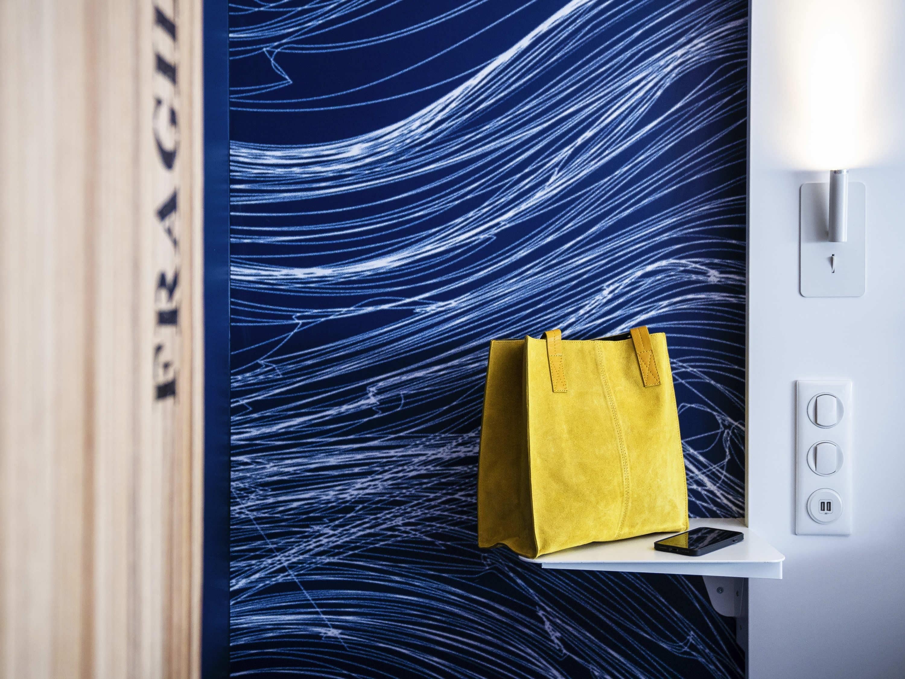 Una habitación con una pared decorada con un diseño abstracto azul, un bolso amarillo sobre una superficie blanca y un interruptor de luz.
