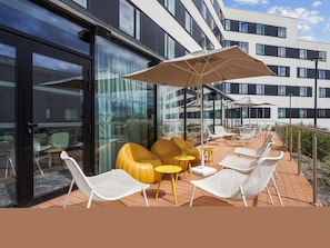 An outdoor seating area with chairs and tables, a large umbrella, and a building with large windows in the background.
