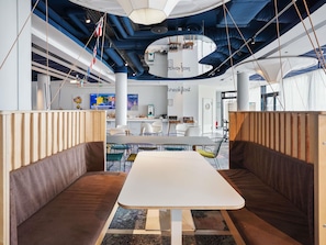 Un interior moderno con una mesa blanca central, zonas de estar y una cocina a la vista.