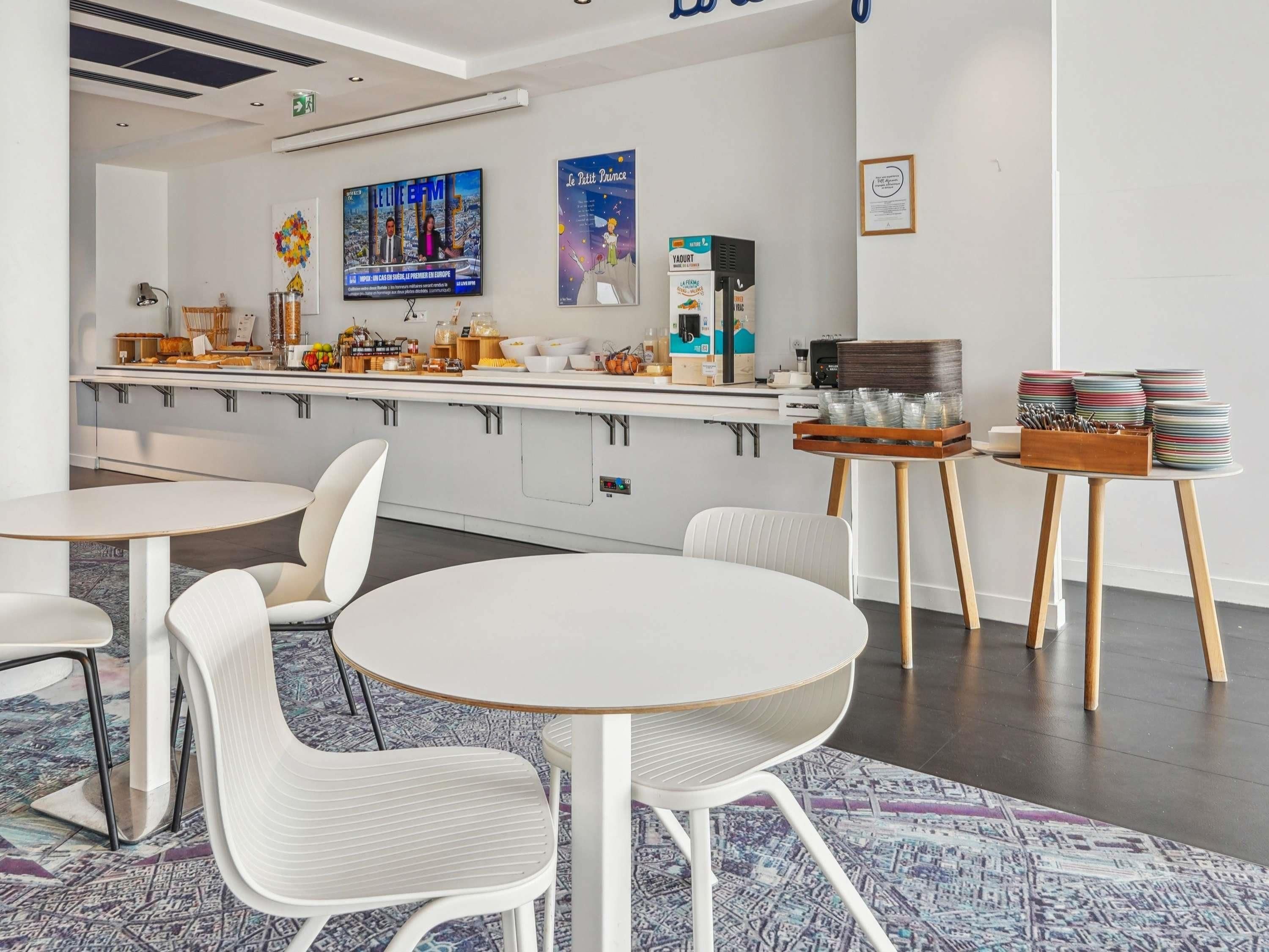 A modern kitchen area with a bar, white chairs, and a coffee machine.
