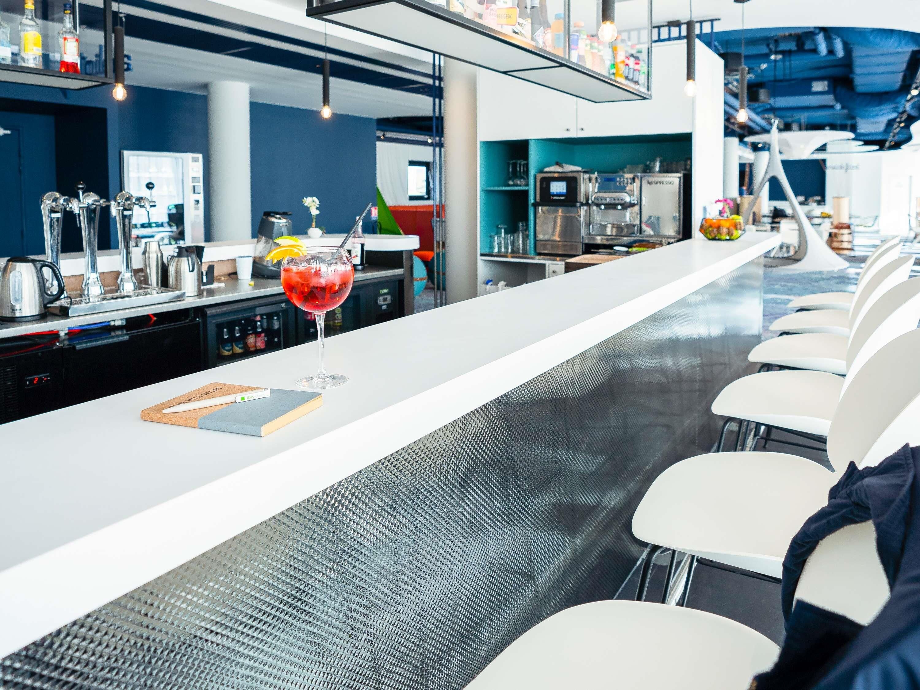 Een moderne bar met een lange toonbank, barstoelen en een cocktailglas.