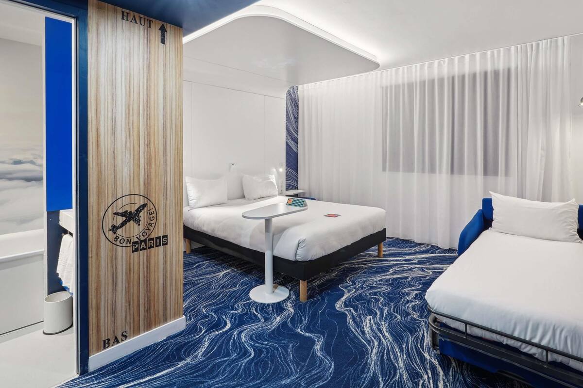 Una habitación de hotel moderna con una cama, mesita de noche y vistas al cielo a través de una ventana.
