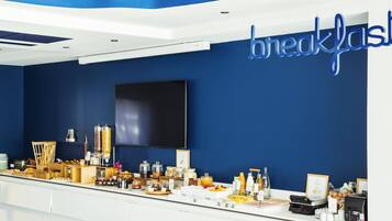 A breakfast buffet with various food items and a large TV screen on the wall.