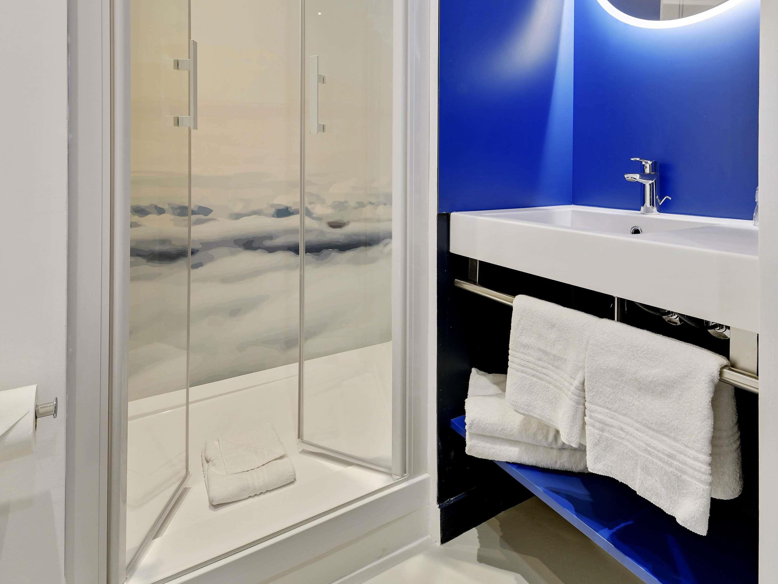 Une salle de bain avec une douche à parois de verre, un lavabo blanc et un mur d’accent bleu.