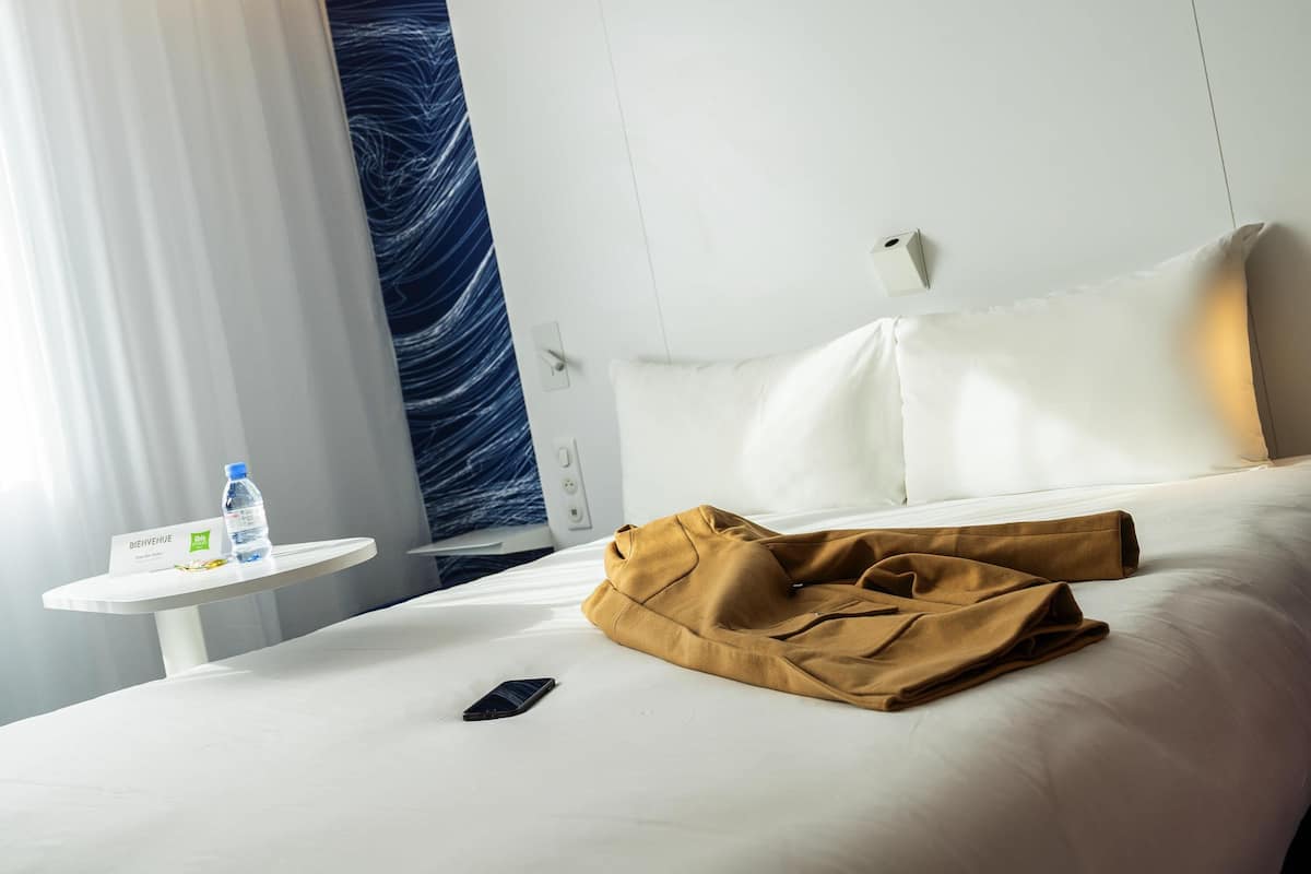 Ett hotellrum med en säng, ett nattduksbord med en vattenflaska, en smartphone och en välkomstskylt.