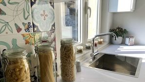 A kitchen with pasta jars on the counter, a sink, and a window with a view of the outside. - The Mori's House, a house in the center close to the sea (Catania)