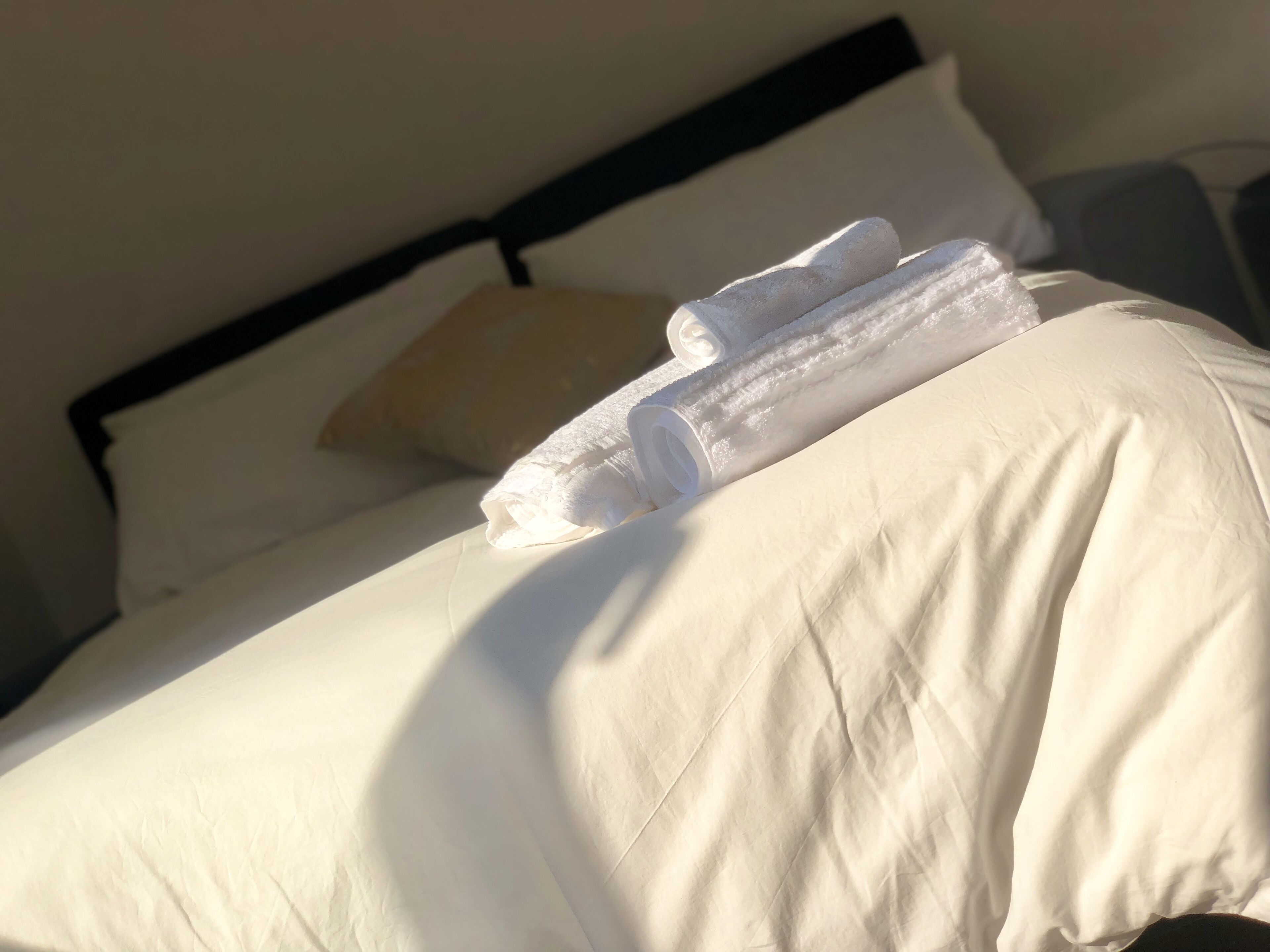 Un lit bien fait, avec des draps blancs et une serviette enroulée posée sur le dessus.