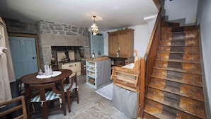 A rustic kitchen with a stone fireplace, wooden cabinets, and a dining area with a table and chairs. - Carrowcullen, The Old Irish Farmhouse (Skreen, Ireland)