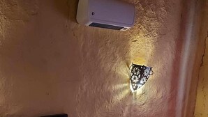 Un dormitorio con cama, mesita de noche, aire acondicionado de pared y una lámpara decorativa en la pared.