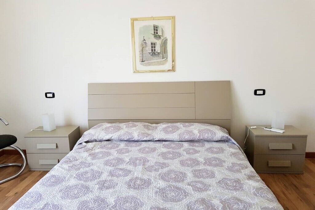 Une chambre à coucher avec un lit, deux tables de chevet, une chaise et un tableau encadré au mur.